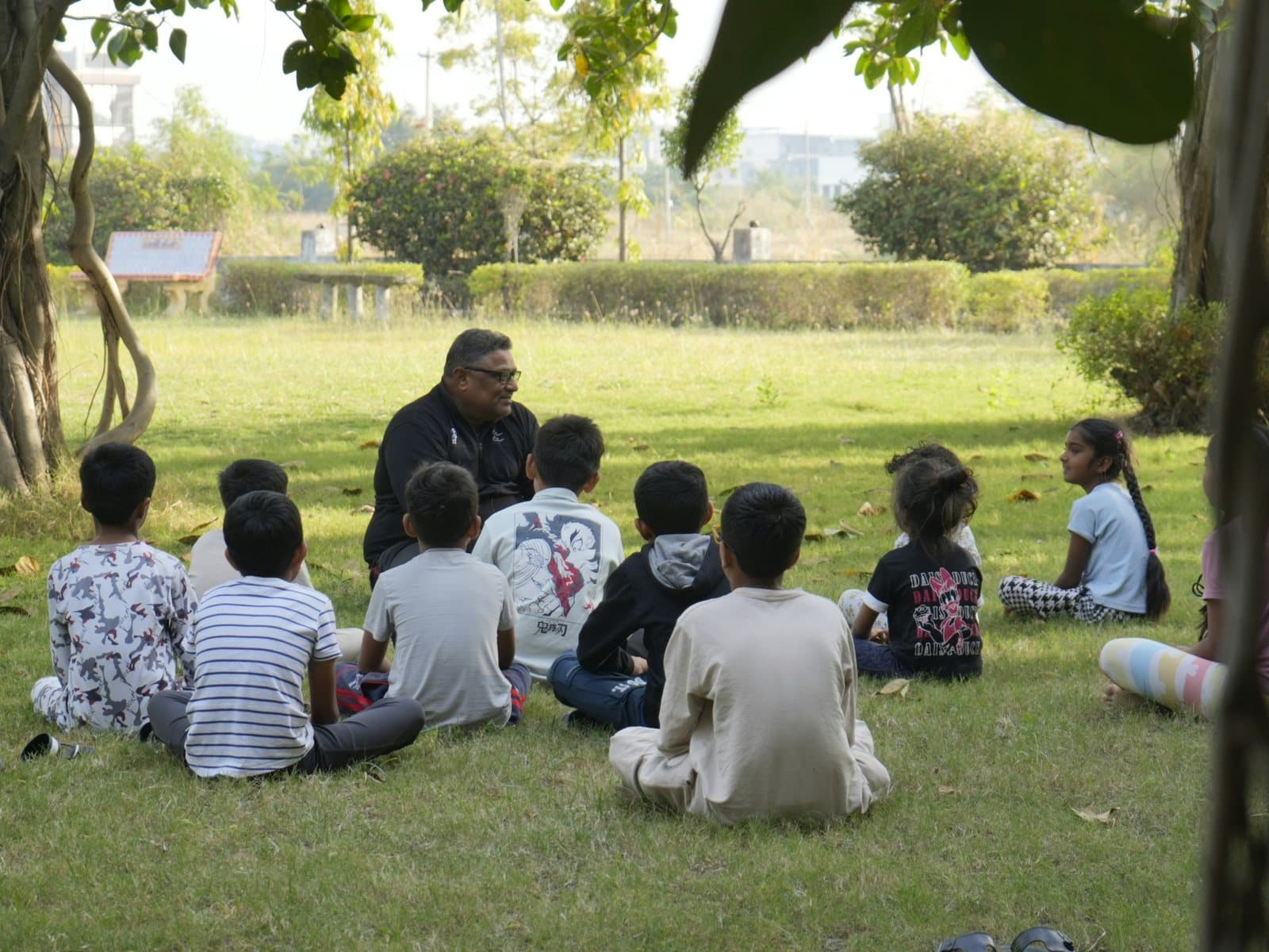 A teacher seated outdoors with a group of children